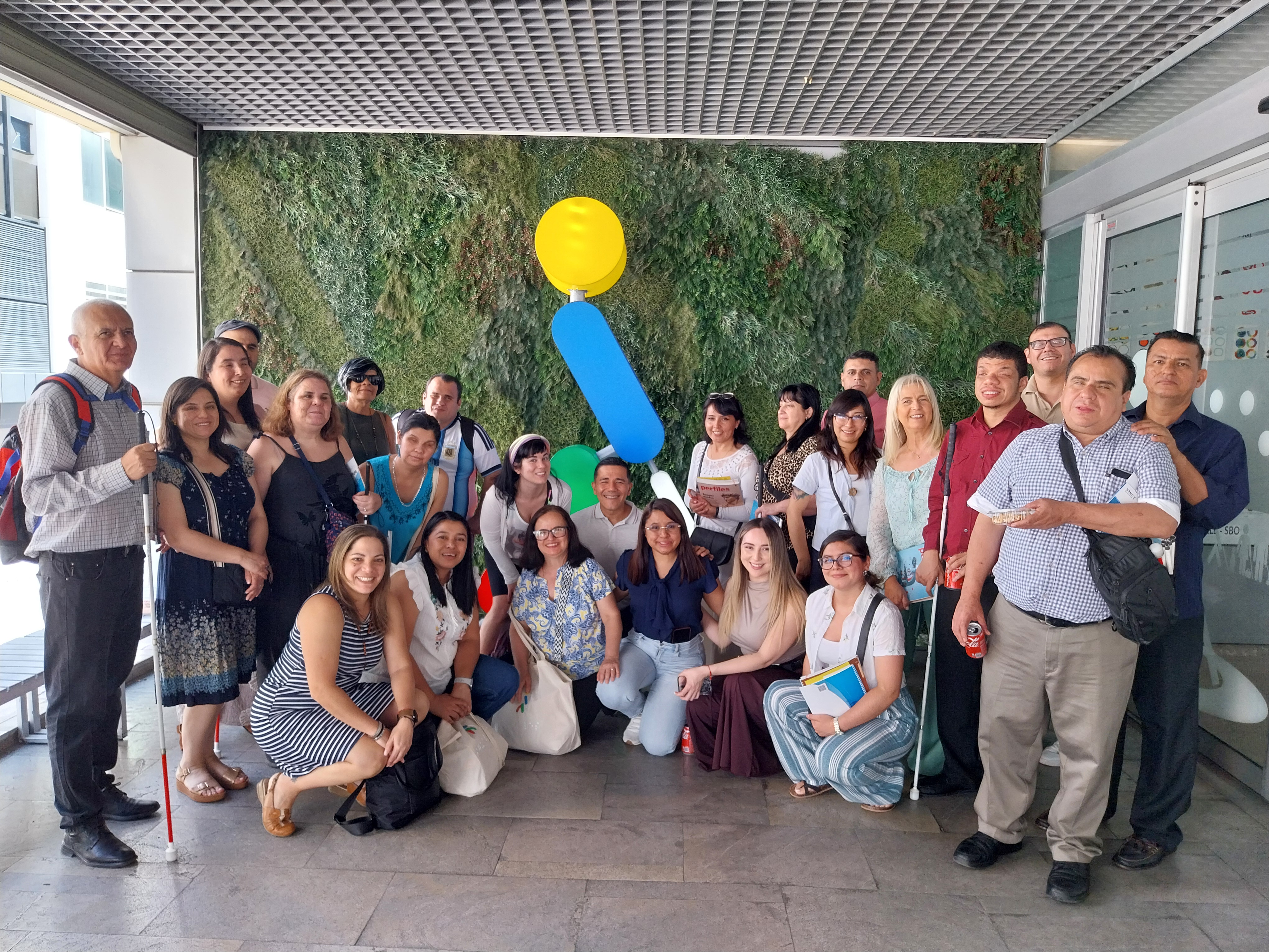 Fotografía muestra a los participantes en la entrada del SBO de la ONCE en Madrid, detrás de ellos está ONCELIO el símbolo de la ONCE