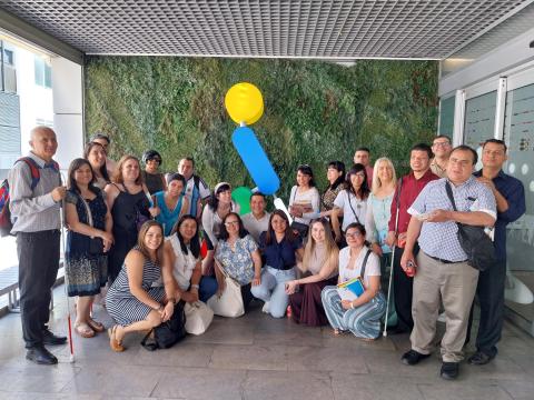 Fotografía muestra a los participantes en la entrada del SBO de la ONCE en Madrid, detrás de ellos está ONCELIO el símbolo de la ONCE